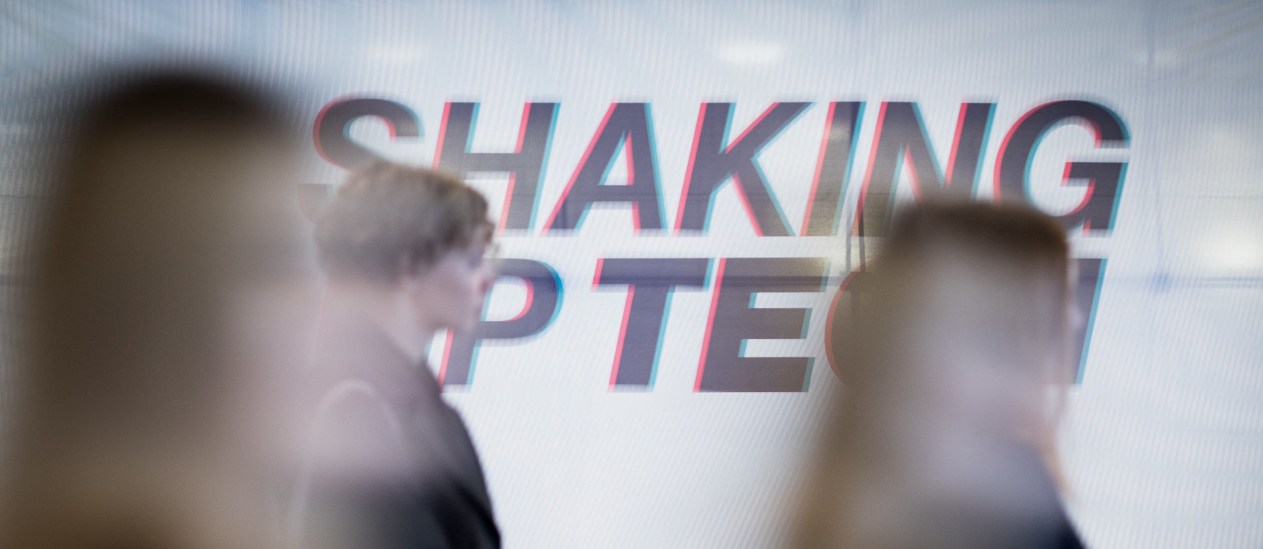 Sumennettu kuva ihmisistä, Shaking up Tech -logo taustalla